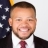 Dr. Marvin Carr, a Black man with a beard wearing a red tie in front of the American flag